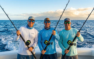 Three smiling anglers on a moving sport fishing boat hold up their Eat My Tackle deep sea rods, with a wide blue ocean and distant sunlit clouds in the background.